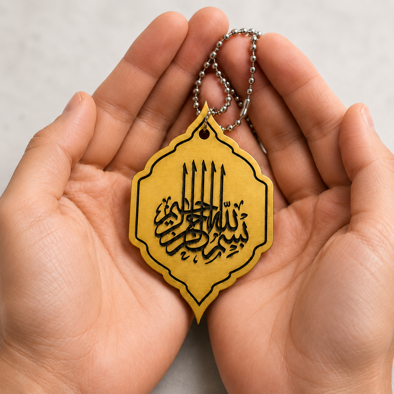 Yellow and black Bismillah Car Pendant held in hands against a neutral background